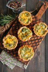 Savory mini quiches (tarts) on a wooden board. Flaky dough pies. Fresh rosemary and dry thyme on a wooden background.