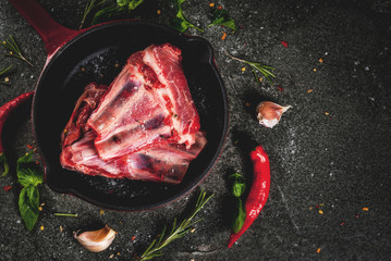 Raw fresh meat, uncooked lamb or beef ribs with hot pepper, garlic and spices in frying pan skillet on dark stone background, copy space top view