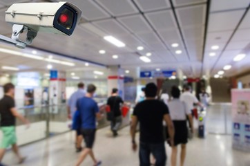 CCTV security indoor camera system operating with blurred image of people walking at train station,...