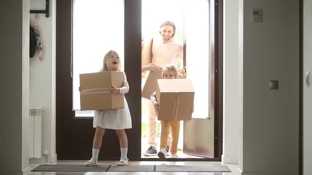 Happy family with kids holding boxes entering new modern house, excited couple and children relocating carrying belongings, opening entrance door looking around while moving in own bought rented home