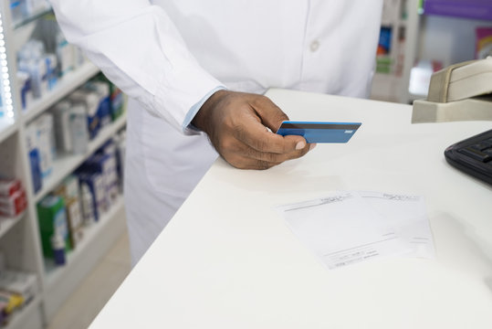 Chemist Holding Credit Card At Counter In Pharmacy