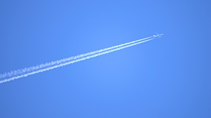Engine exhaust contrails forming behind flying commercial airplane