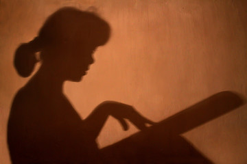 Silhouette of a girl with a tablet in hand on a brown orange background. A woman is walking her finger along the screen of the gadget.