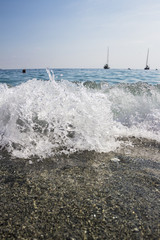 Close up shot of small breaking waves on the beach side. Lovely small surge with sand and boats, blue ocean water and boats in the background horizon. - 175477104