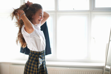Teenage schoolgirl styling long hair in bedroom