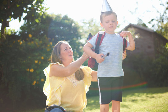 Mature woman putting rocket costume backpack onto son  in garden