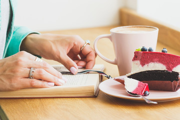 Woman with a cup of cappuccino and a piece of dessert on the plate