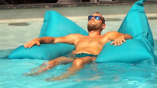 Young man sunbathing on air mattress in pool, super slow motion 240fps
