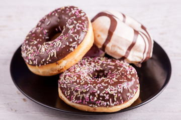 Delicious donuts in a black plate over white wooden background