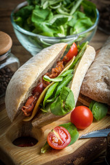Ciabatta sandwich with arugula salad, bacon and yellow cheese.