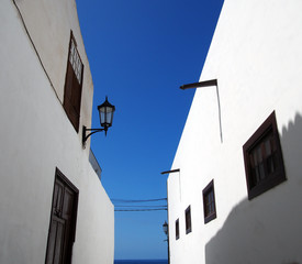 Fototapeta na wymiar street of traditional white houses in perspective view looking upwards with bright blue summer sky leading to the sea