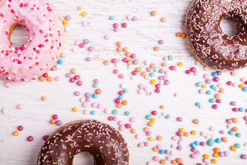 Overtop view of donuts in and sweet candy on white wooden background. Delicious junk food
