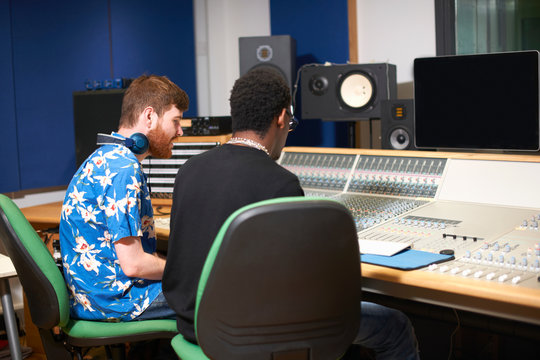 Two young male college students at sound mixer in recording studio