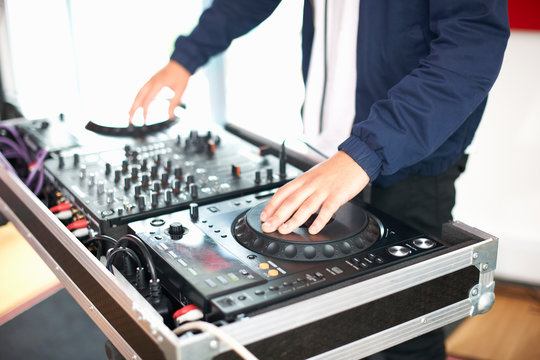 Young male college student spinning DJ turntables in recording studio