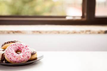 Close up of Plate with donuts next to window sill. Delicious junck food