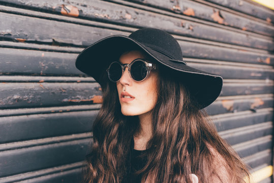 Portrait of young woman standing beside shutter, wearing floppy hat and sunglasses