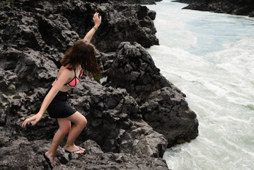 Teenage girl stands on coastal stones near river