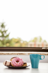 Donuts and a cup of coffee next tot the window sill. Delicious junck food