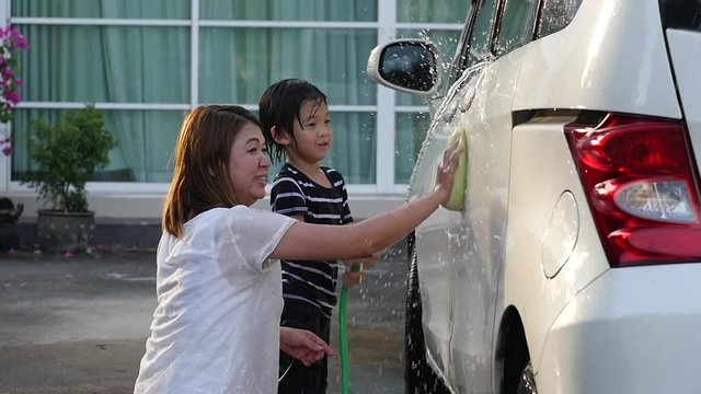 Asian mother and son washing car together on summer day slow motion 