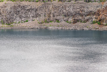 The rocky shore of an abandoned and submerged quarry with blue water