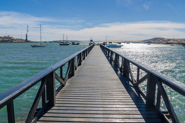 Wooden pier leading out into bay on sunny day with many boats, Luderitz, Namibia, Southern Africa