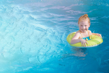 Happy little girl bathes in blue water on an inflatable yellow circle