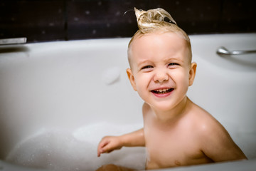 Little cute boy bathes in a bath and plays with foam
