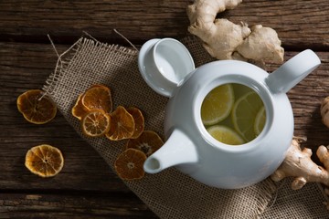 Lemon slice in teapot with ginger and dried orange on wooden