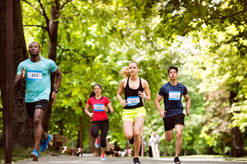 Group of young athletes running in green sunny park.