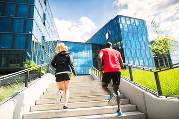 Young couple running in front of glass buildings.