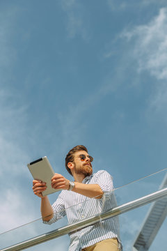 Young Caucasian businessman using a digital tablet in front of a corporate building.
