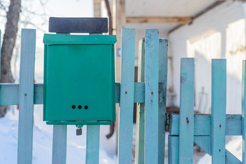 Closeup image of vintage rusty metal mail box hanging on blue wooden fence at green summer background.