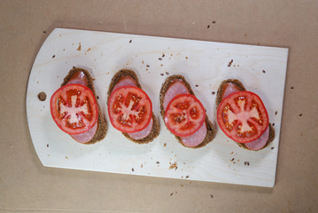 evenly sliced brown bread with tomatoes on wooden board for cutting
