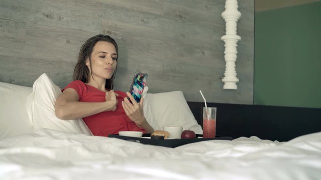 Happy woman taking photo of food during breakfast in bed at home
