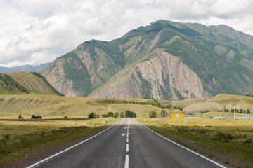 Asphalt road with a marking going to the foot of high mountains with clouds in the background