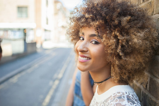 Portrait of young woman leaning against wall, smiling