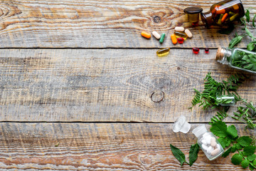 Healing herbs. Fresh leaves, bottles and pills on wooden background top view copyspace