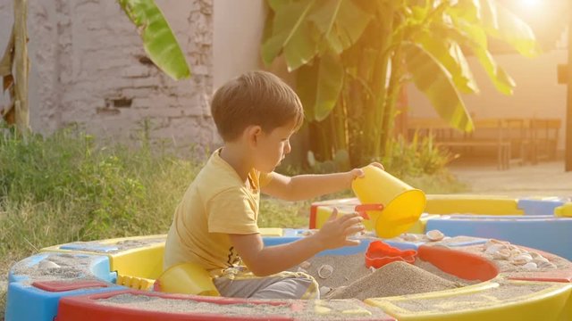 Cute boy playing with sand in a sandbox