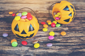 Halloween pumpkin face buckets with colorful candy inside on old wooden texture
