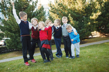 Happy school children in uniform and with backpacks holding hands and jumping in the park, back to school