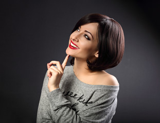 Obraz premium Myśląca kobieta biznesu makijaż patrząc z toothy naturalny uśmiech na ciemnoszarym tle. Krótkie włosy. Zbliżenie