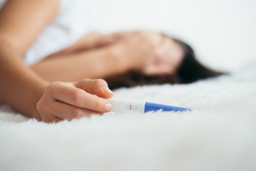 Obraz na płótnie Canvas Upset woman lie sad in the bed with negative pregnancy test