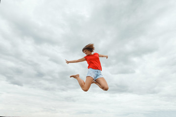 fitness, sport, victory, success and healthy lifestyle concept - happy woman winning and coming jumping in air over sky background
