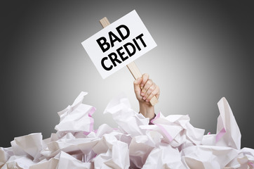 Bad credit  placard in hand with crumpled paper pile. Concept of bad financial situation.
