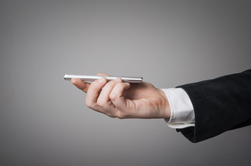 An elegant businessman`s hand holding a smart phone in front of an empty clear gray wall background concept