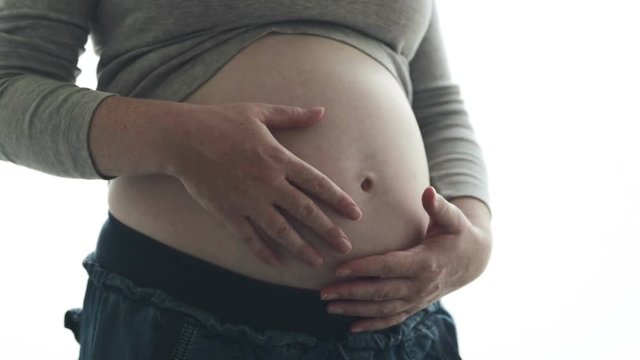 Pregnant woman touching and rubbing her belly, mother stroking and stimulating abdomen, adult caucasian female in fifth month or twenty first week of pregnancy (second trimester)