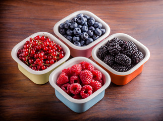 Berries mix of red currants, blueberries, blackberries and raspberries in four colorful ceramic jars on brown wooden table in studio