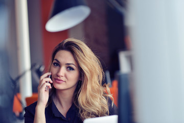 Happy beautiful young business woman sitting and talking on cell phone in office