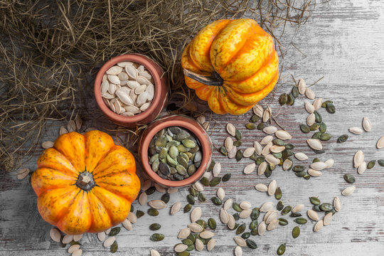 Pumpkins colorful group and seeds overhead in two ceramic jars on white rustic table with straw in studio