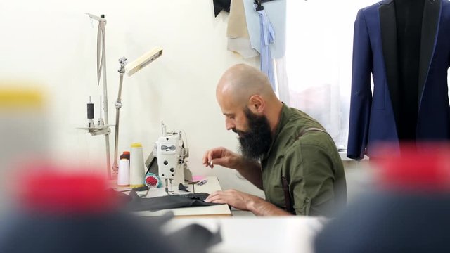 The tailor begins to draw a pattern on the gray material with white chalk.